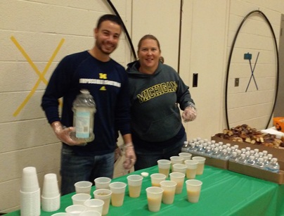 Two teachers pose for the camera as they continue to full up juice cups.