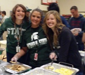 Three teachers smile bright as they hold up some scrambled eggs and pancakes.