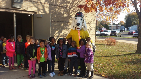 Brookwood students gather around the Firefighter's mascot. A dalmatian dog wearing a yellow shirt, orange tie and a hat.