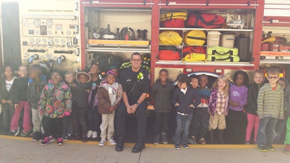 Students stand with a firefighter beside his truck. We can see all the equipment the fire fighters use!