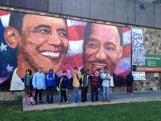 Students stand in front of a mural that shows Obama and Martin Luther King Jr on it.