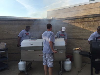 A few dads standing around a large grill while cooking up some delicious food!