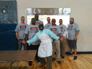 A group of dads stand together with the Principal to show off their dad's grilling shirts.