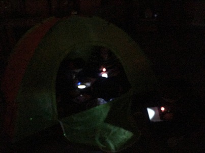 Three kids gather in and around a tent to read.